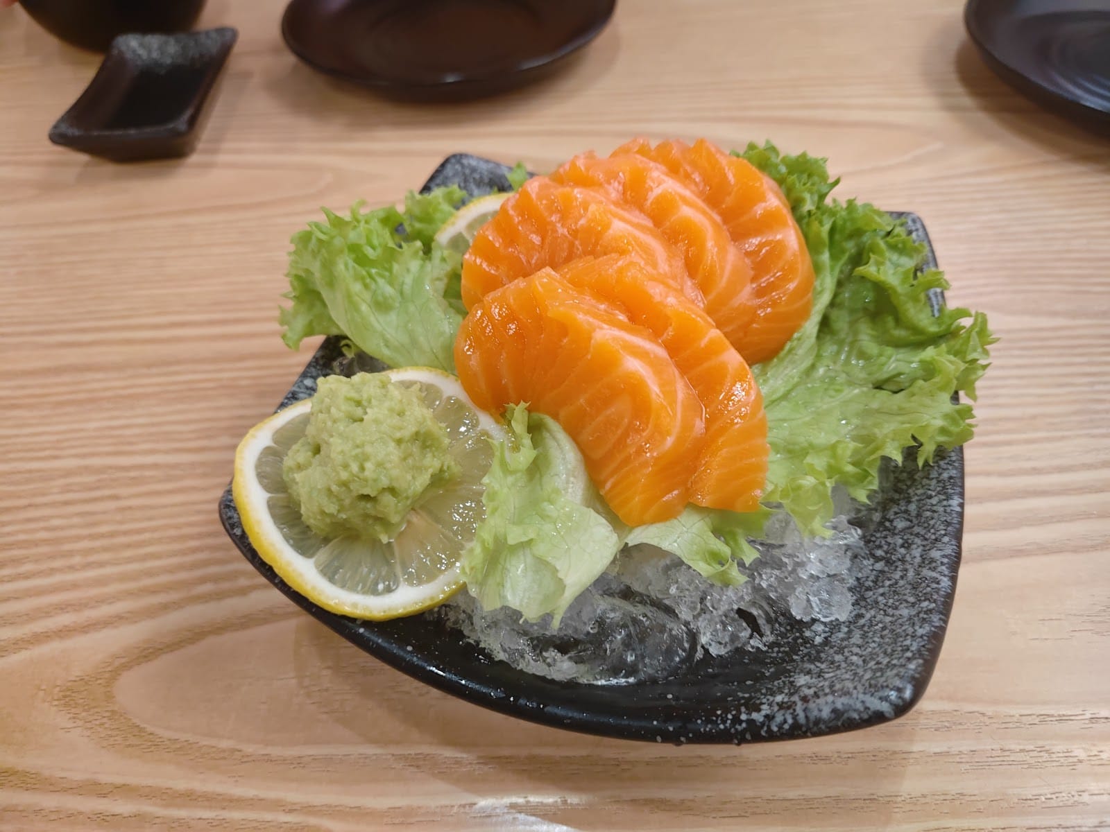 Salmon sashimi on ice with lettuce, lemon and wasabi
