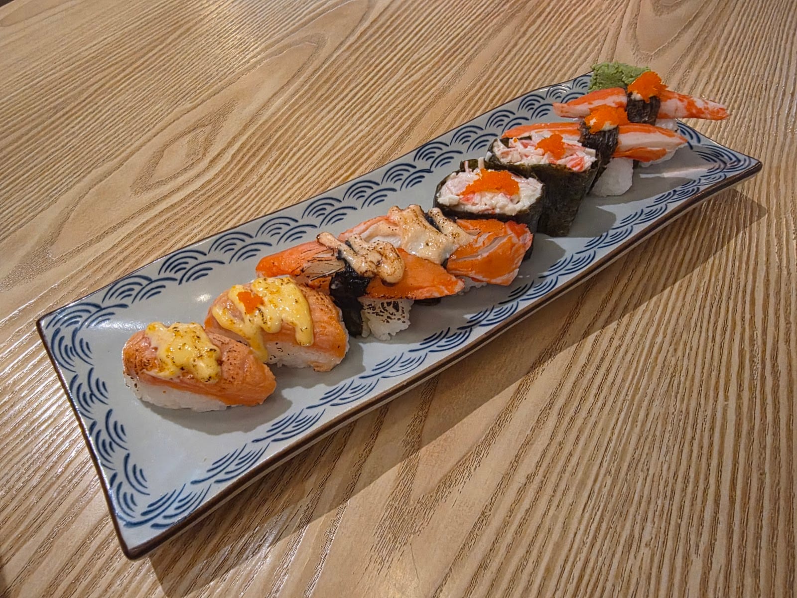 A long plate of seared salmon sushi, crab stick nigiri and gunkan