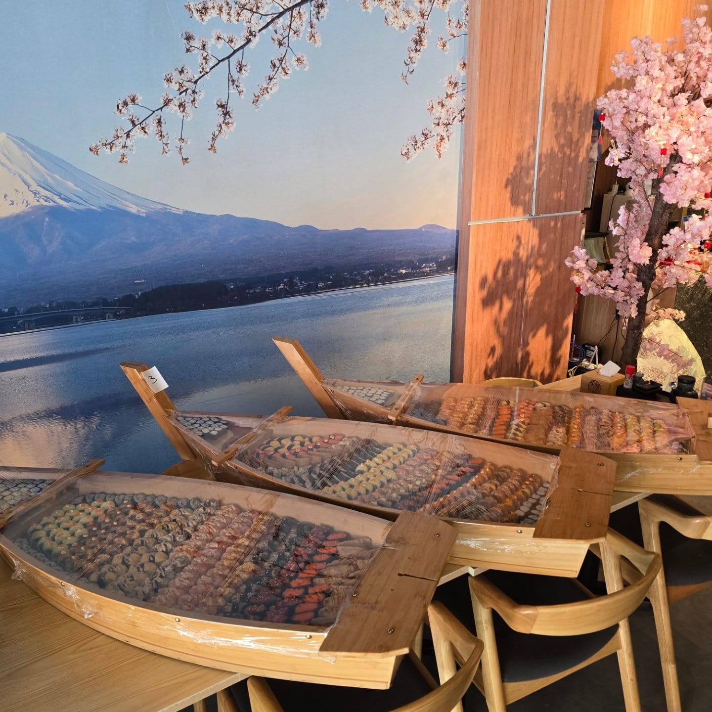 Three wooden sushi boats, wrapped and ready, in front of Hanazen's Mount Fuji mural